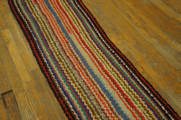 Braided runner rug featuring vibrant multicolored stripes sits on light, worn hardwood planks.