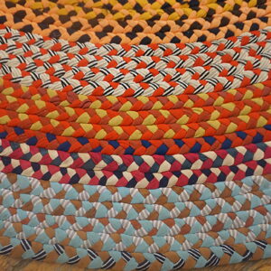 Concentric bands of bright, multicolored braids form a round rug lying on rustic wood flooring.