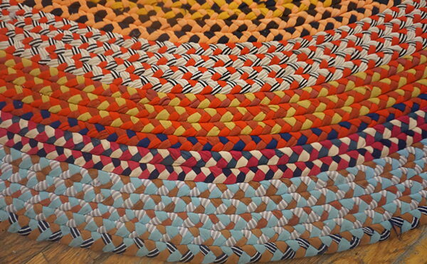 Concentric bands of bright, multicolored braids form a round rug lying on rustic wood flooring.