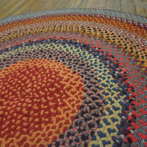 Multicolored braided round rug featuring red, orange, blue, and yellow rings on rustic wood floors.