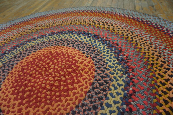 Multicolored braided round rug featuring red, orange, blue, and yellow rings on rustic wood floors.