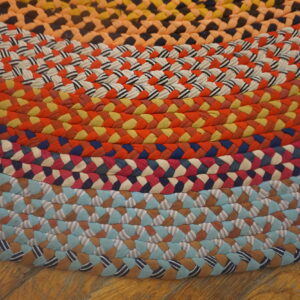Brightly colored braided rug showing concentric rings of orange, blue, red, and striped patterns on wood flooring.