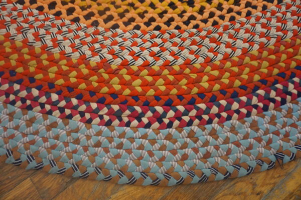 Brightly colored braided rug showing concentric rings of orange, blue, red, and striped patterns on wood flooring.