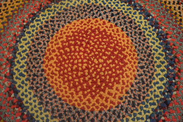 Multicolor braided round rug with concentric bands of red, orange, yellow, blue, and patterned braids.