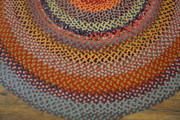 Close view of a thick multicolor round braided rug on light brown hardwood flooring.