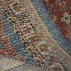 Low-pile rug with intricate red, blue, and tan traditional patterns rests on distressed wood flooring.