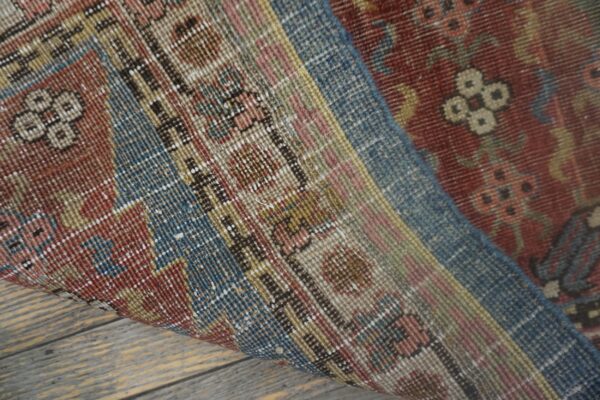 Low-pile rug with intricate red, blue, and tan traditional patterns rests on distressed wood flooring.