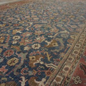 Traditional blue rug featuring detailed floral motifs in faded pink, beige, olive, and a wide red border.