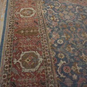 Distressed traditional rug with blue field and red border on worn light brown plank flooring.