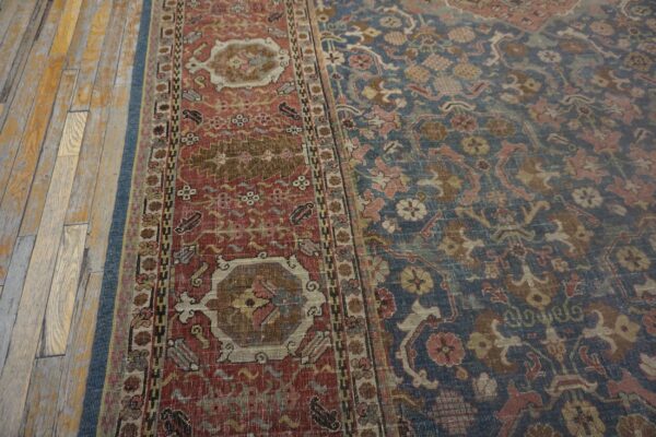 Distressed traditional rug with blue field and red border on worn light brown plank flooring.