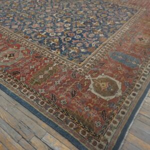 Ornate blue and red patterned rug with low pile and wear rests on heavily distressed wooden plank flooring.