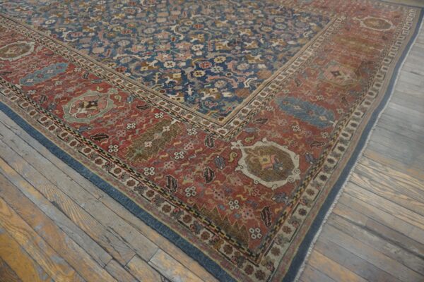 Ornate blue and red patterned rug with low pile and wear rests on heavily distressed wooden plank flooring.