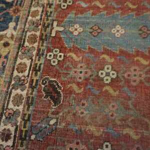 Woven rug detail showing red, navy, and teal patterns, including stylized motifs and a multi-striped border.