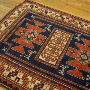Geometric navy blue, red, and cream rug with stylized medallions rests on plank wood flooring.