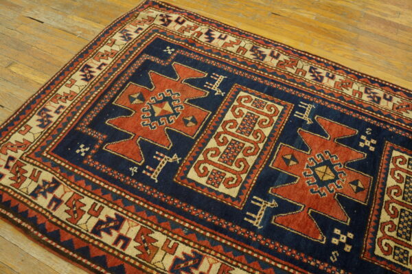 Geometric navy blue, red, and cream rug with stylized medallions rests on plank wood flooring.