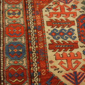 Textured rug detail with bold geometric patterns in rust red, blue, and cream on a wood floor.