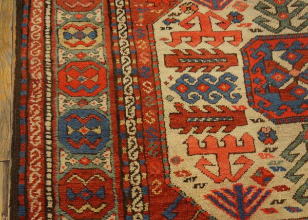 Textured rug detail with bold geometric patterns in rust red, blue, and cream on a wood floor.