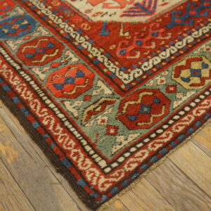 Red, teal, and cream geometric patterned rug corner rests on rustic wide plank wood flooring.