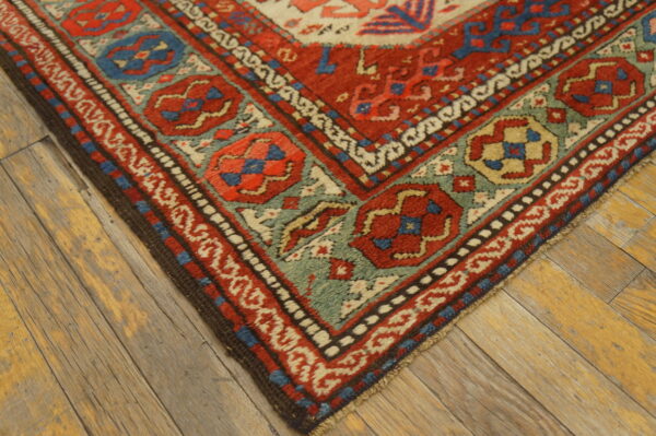 Red, teal, and cream geometric patterned rug corner rests on rustic wide plank wood flooring.