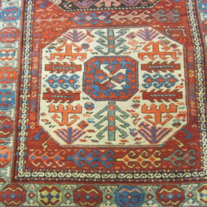 Low-pile rug with a complex geometric pattern in deep red, blue, teal, and cream on hardwood flooring.