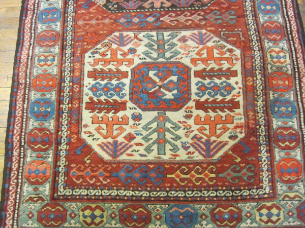 Low-pile rug with a complex geometric pattern in deep red, blue, teal, and cream on hardwood flooring.