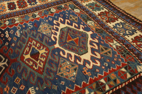 Detailed low-pile rug with geometric medallions and borders in navy, red, cream, and teal on wood flooring.
