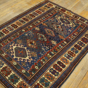 A geometric tribal rug featuring blue, red, and cream patterns lies flat on light wooden flooring.
