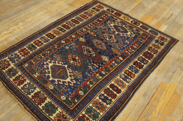A geometric tribal rug featuring blue, red, and cream patterns lies flat on light wooden flooring.