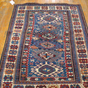 Rectangular rug with blue, red, and cream tribal geometric patterns lies on glossy hardwood planks.
