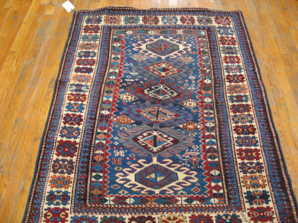 Rectangular rug with blue, red, and cream tribal geometric patterns lies on glossy hardwood planks.