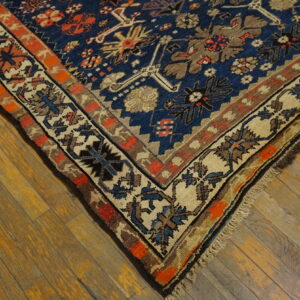 Navy blue geometric rug with rust and beige borders rests on warm, rustic wood floors.