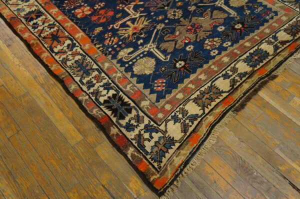 Navy blue geometric rug with rust and beige borders rests on warm, rustic wood floors.