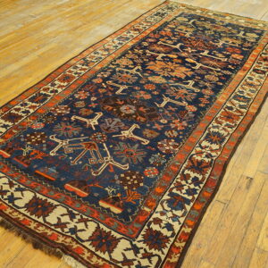 Navy runner rug with geometric designs in rust, cream, and orange on distressed hardwood flooring.