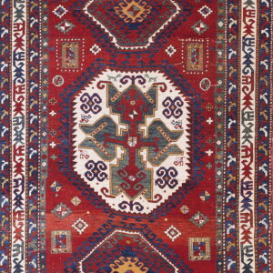Deep red rug with complex geometric patterns in navy blue, cream, and gold across the field and borders.