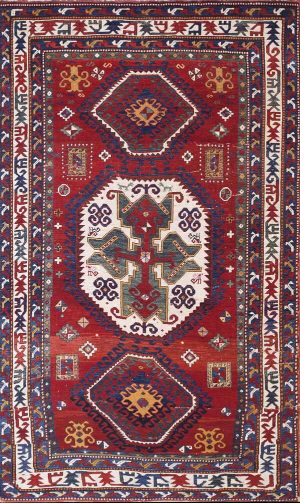 Deep red rug with complex geometric patterns in navy blue, cream, and gold across the field and borders.