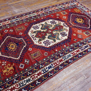 Traditional geometric rug in red, navy, cream, and yellow resting on weathered wood planks.