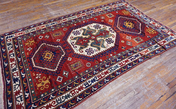 Traditional geometric rug in red, navy, cream, and yellow resting on weathered wood planks.
