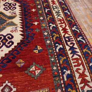 Red, navy, and cream geometric patterned rug with a low pile rests on distressed wood planks.