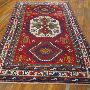 Red rug featuring large white and blue geometric patterns displayed on glossy hardwood flooring.