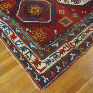 Red rug with bold geometric medallions and multi-colored borders rests on plank wood flooring.