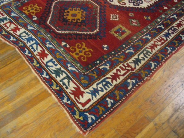 Red rug with bold geometric medallions and multi-colored borders rests on plank wood flooring.