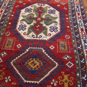 Red, blue, and white geometric tribal rug with a large central medallion on a wooden floor.