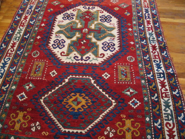 Red, blue, and white geometric tribal rug with a large central medallion on a wooden floor.