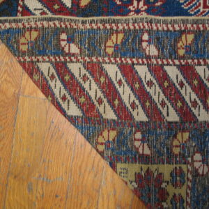 Flatweave rug with red, blue, and cream geometric patterns rests on worn honey-colored hardwood flooring.