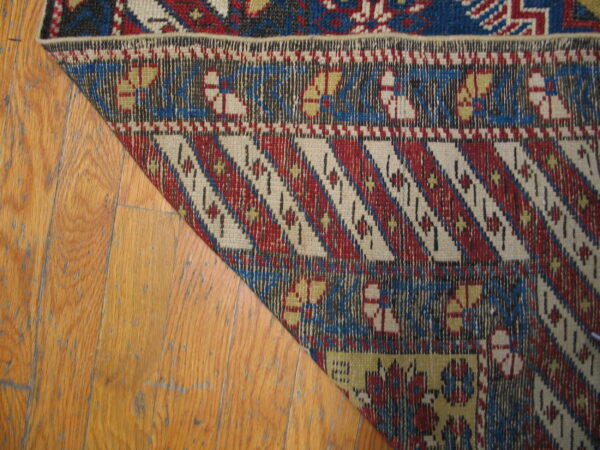 Flatweave rug with red, blue, and cream geometric patterns rests on worn honey-colored hardwood flooring.