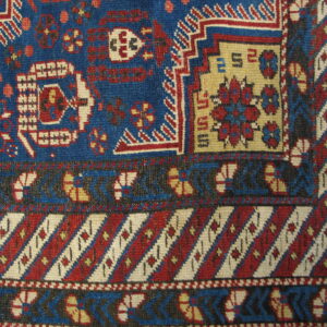 Close-up shows geometric motifs in deep blue, red, cream, and black with complex banded and striped borders.