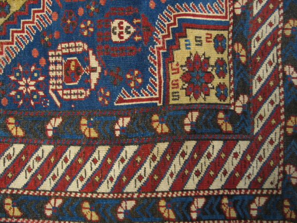 Close-up shows geometric motifs in deep blue, red, cream, and black with complex banded and striped borders.