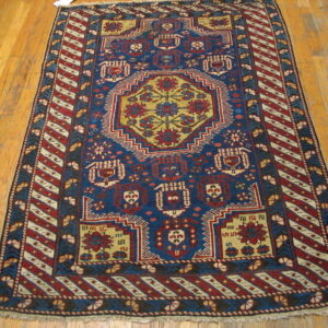 Geometric blue rug with red and mustard yellow medallion and striped borders on hardwood planks.