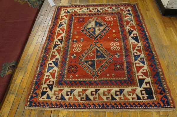 Geometric red rug featuring blue and beige accents and diamond designs on hardwood flooring.