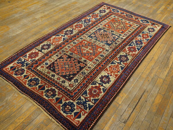 Geometric rug with navy blue, rust orange, and cream repeating medallions on worn wooden flooring.